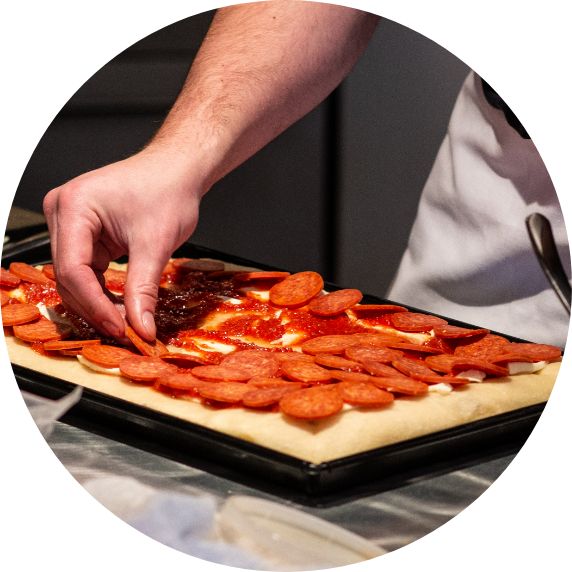 laying pepperoni out on dough in a pan