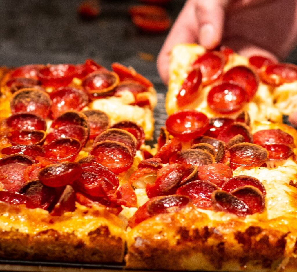 A great looking pepperoni pizza, with a hand reaching to take a slice